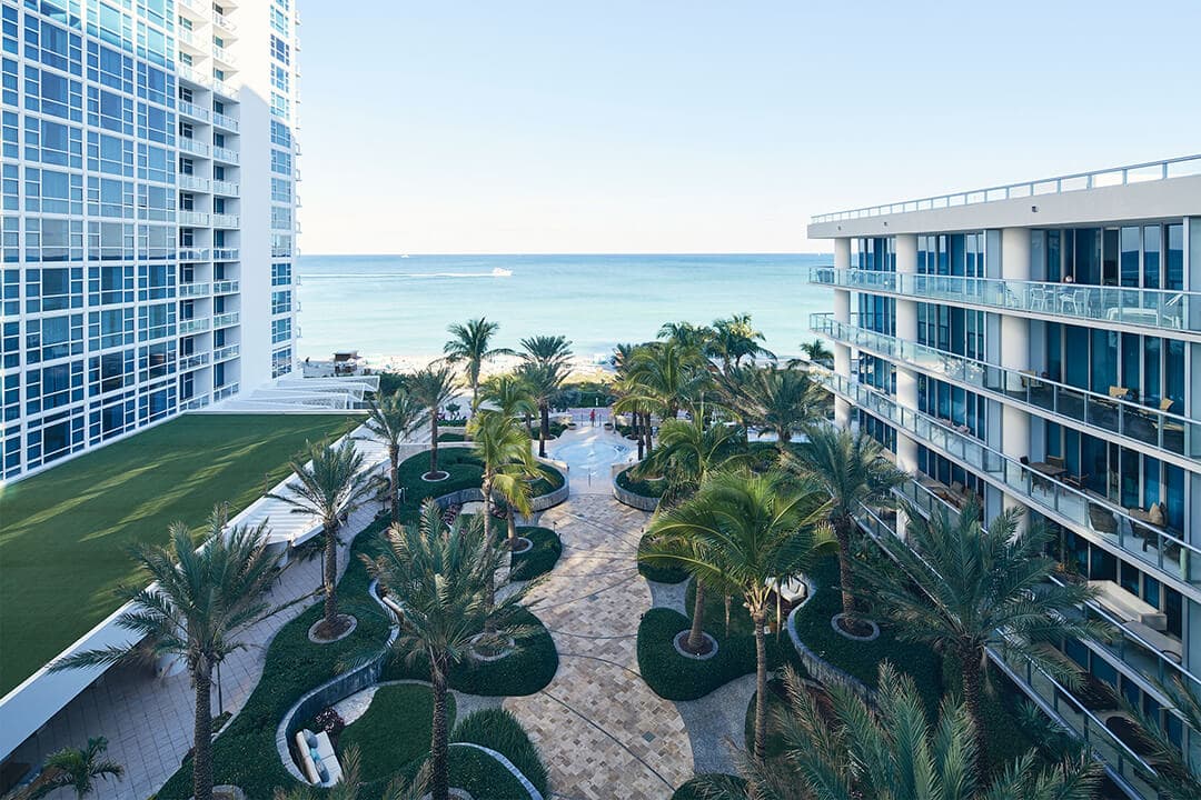 Modern oceanfront resort with palm-lined courtyard and beach view
