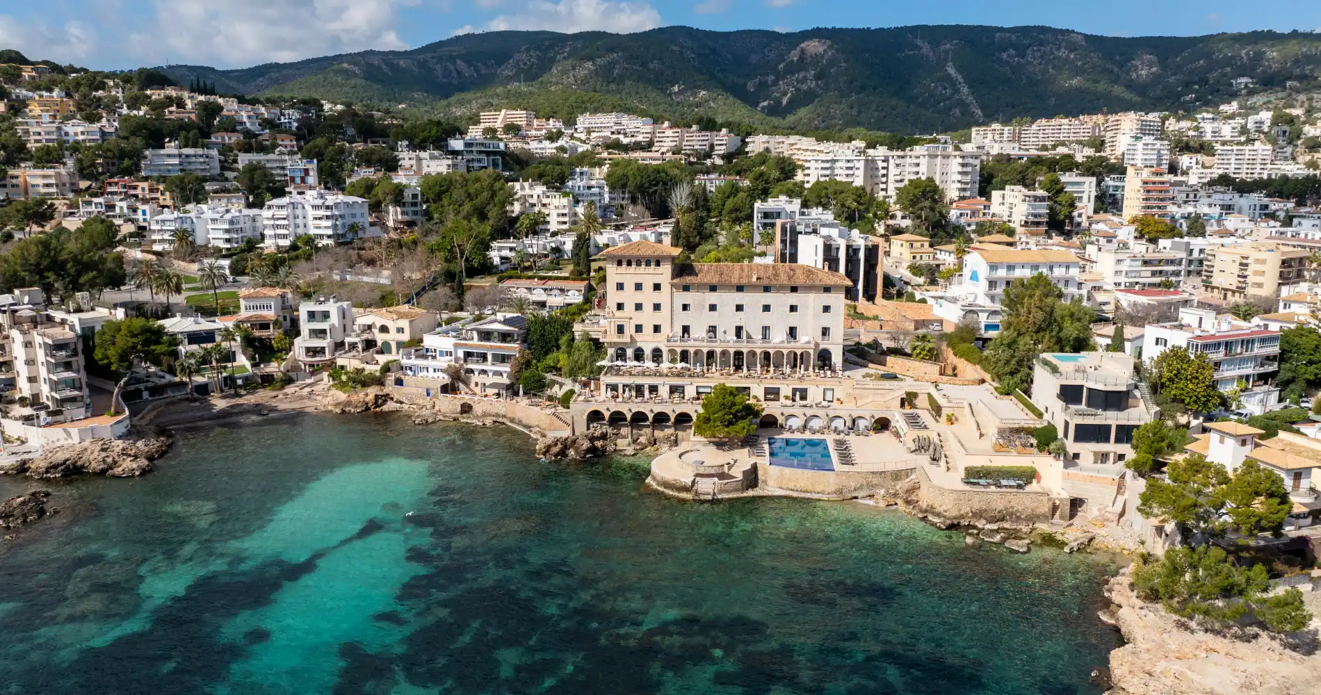 Clifftop Mediterranean resort with turquoise waters, terraced pool, and mountain backdrop