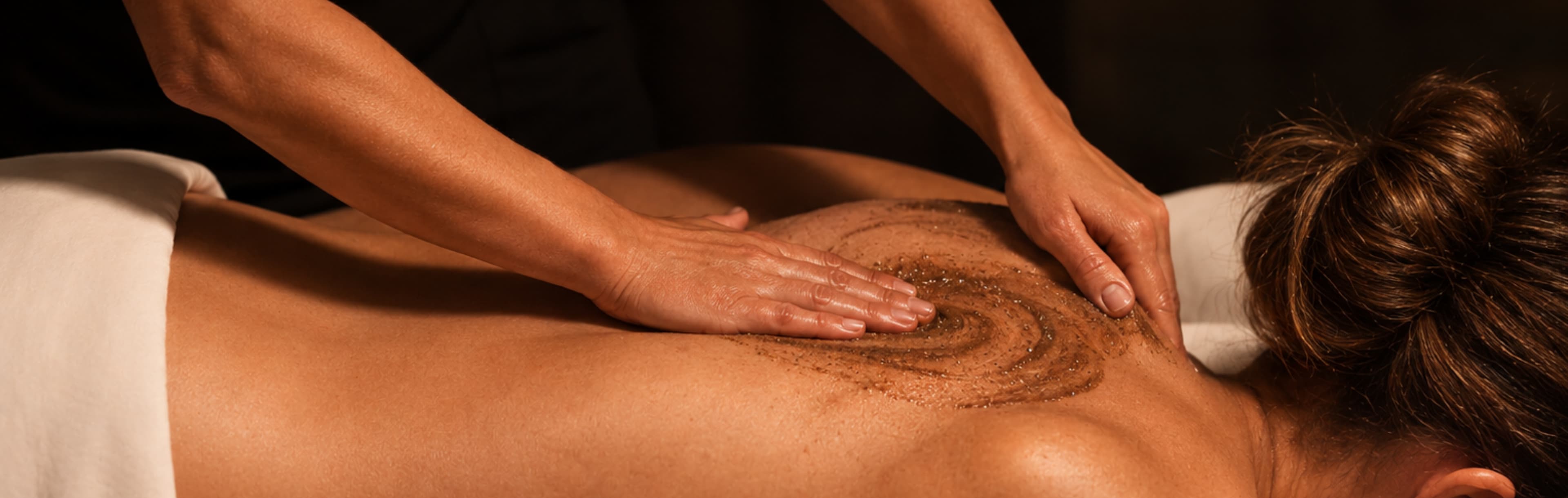 Therapist applying exfoliating body scrub to client's back during spa treatment