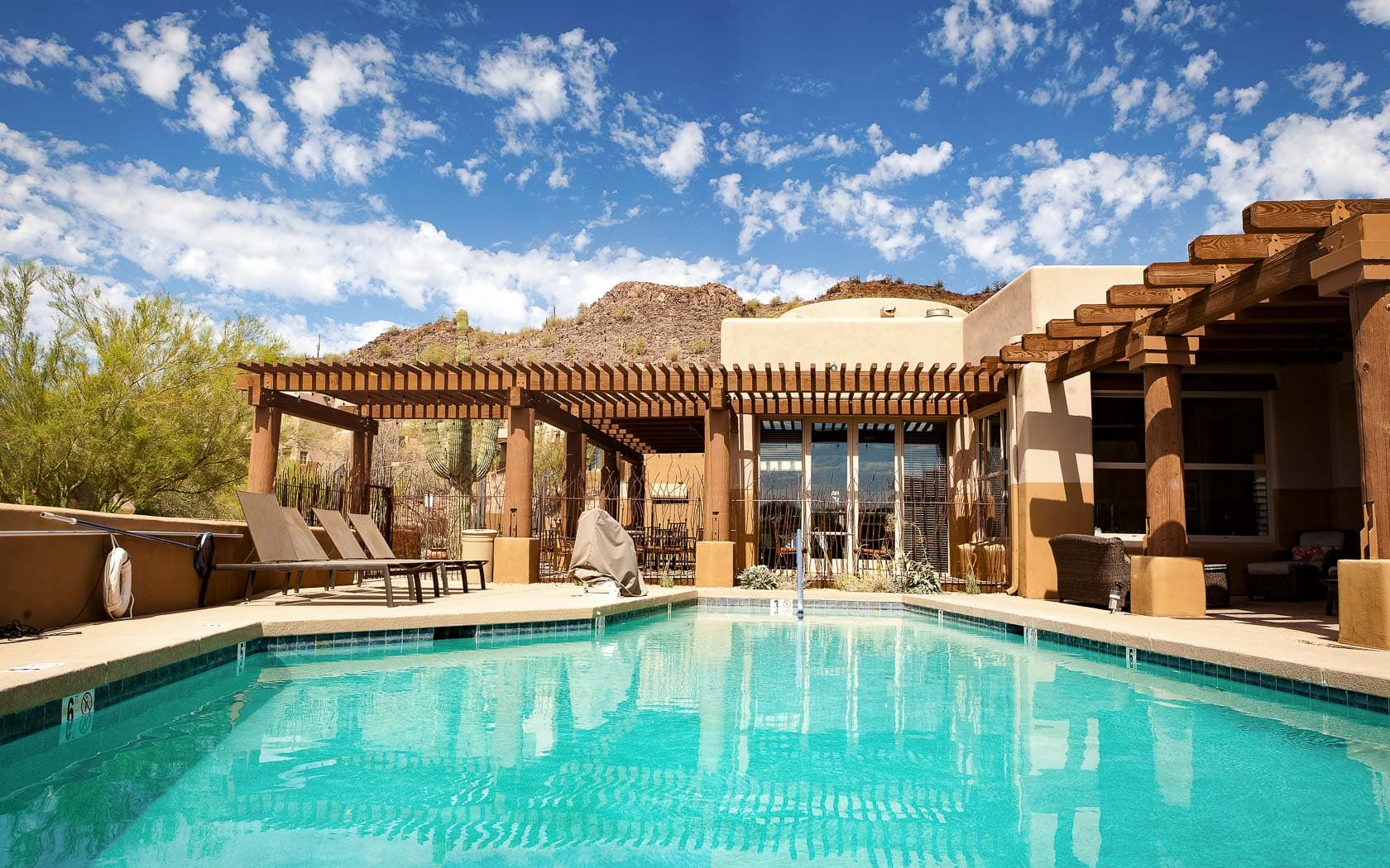 Resort pool with turquoise water, wooden pergolas, and desert mountain views under blue sky