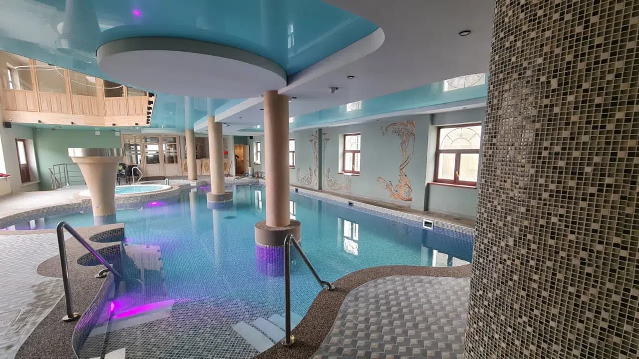 Indoor swimming pool with turquoise water, columns, and blue-lit ceiling