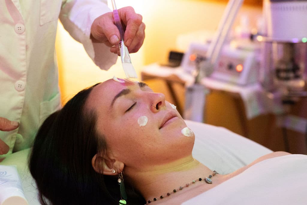 Aesthetician applying facial treatment to client in spa room