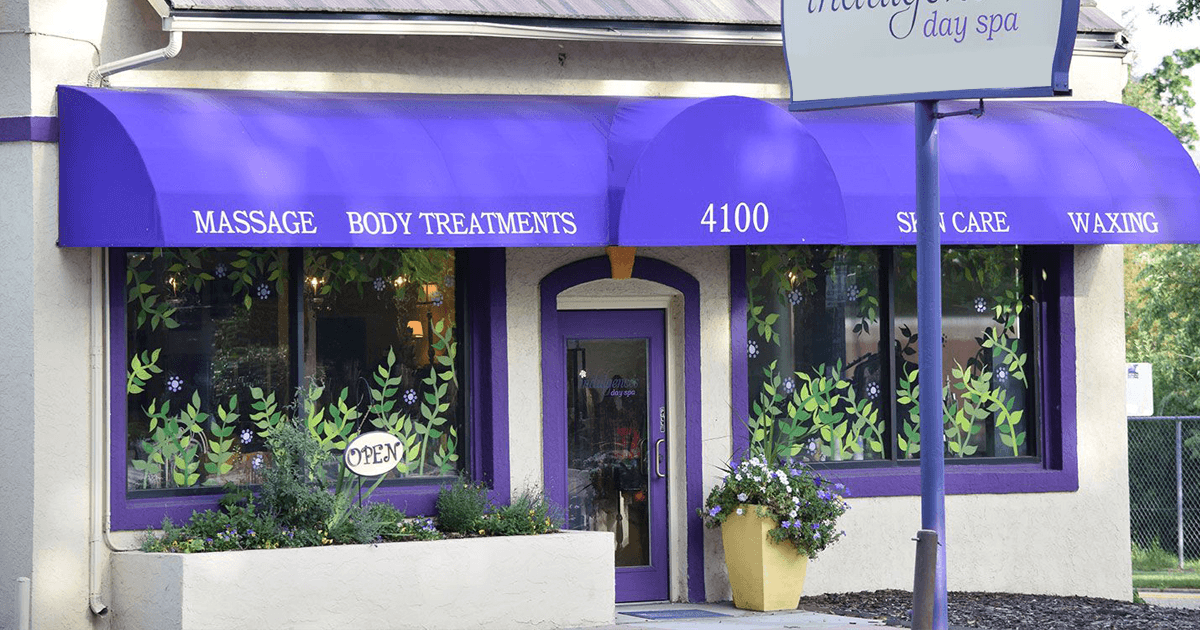Purple storefront with large windows, white trim, flowering planters, and awning sign for Indulgences Day Spa