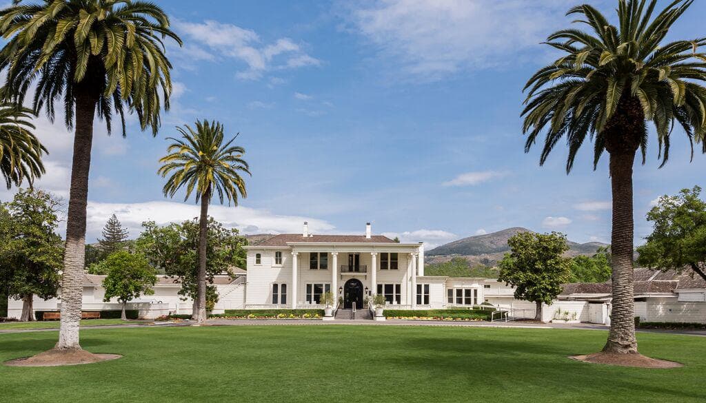 Grand white estate with columned entrance framed by palm trees and manicured lawn