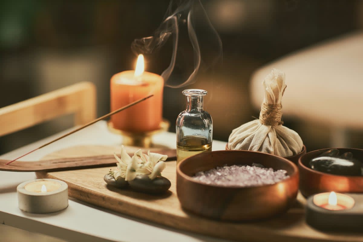 Spa treatment setup with candles, oil bottle, salt bowl, and incense on wooden tray