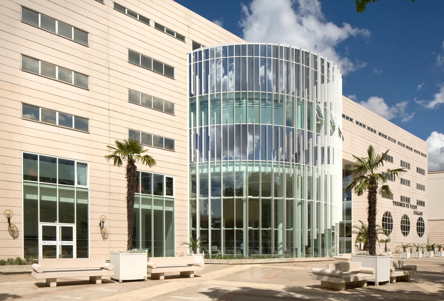 Modern curved glass spa building with cream stone facade and palm trees