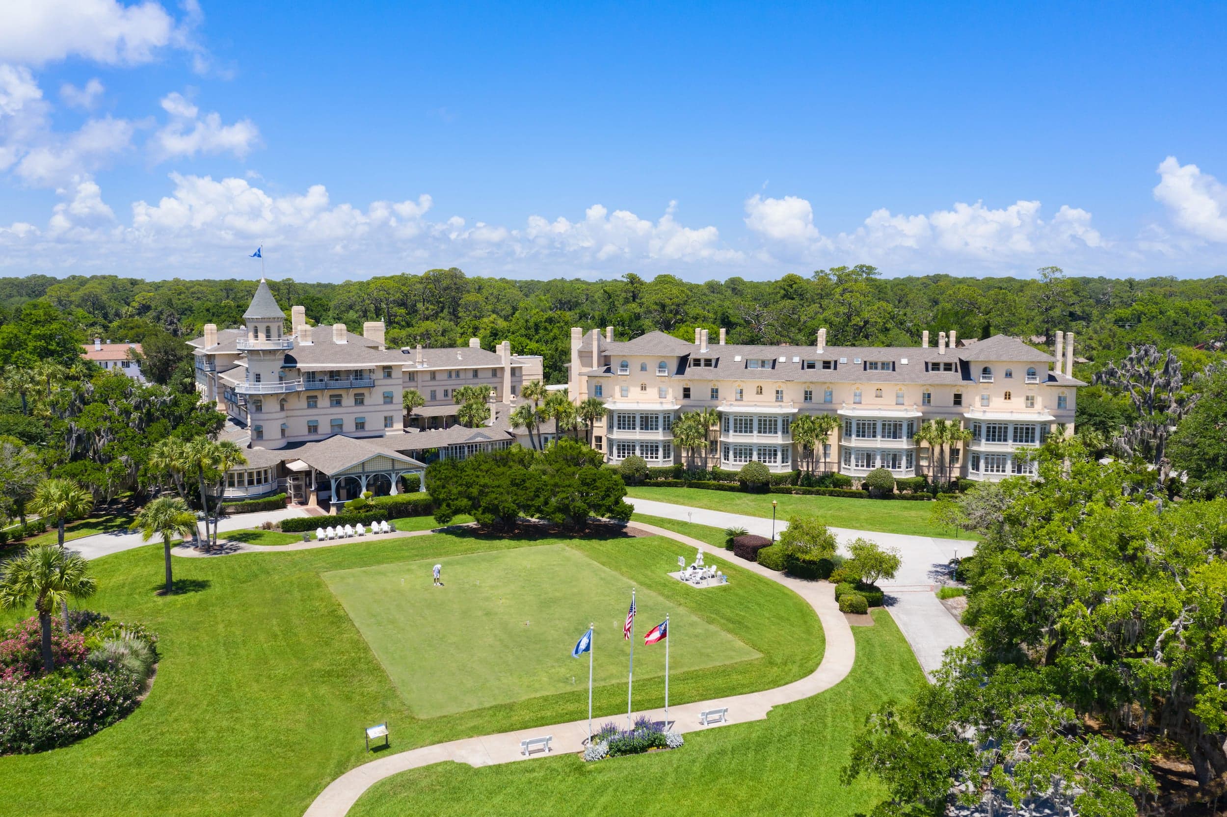 Grand Victorian resort buildings with manicured grounds, palm trees, and flags overlooking coastal landscape