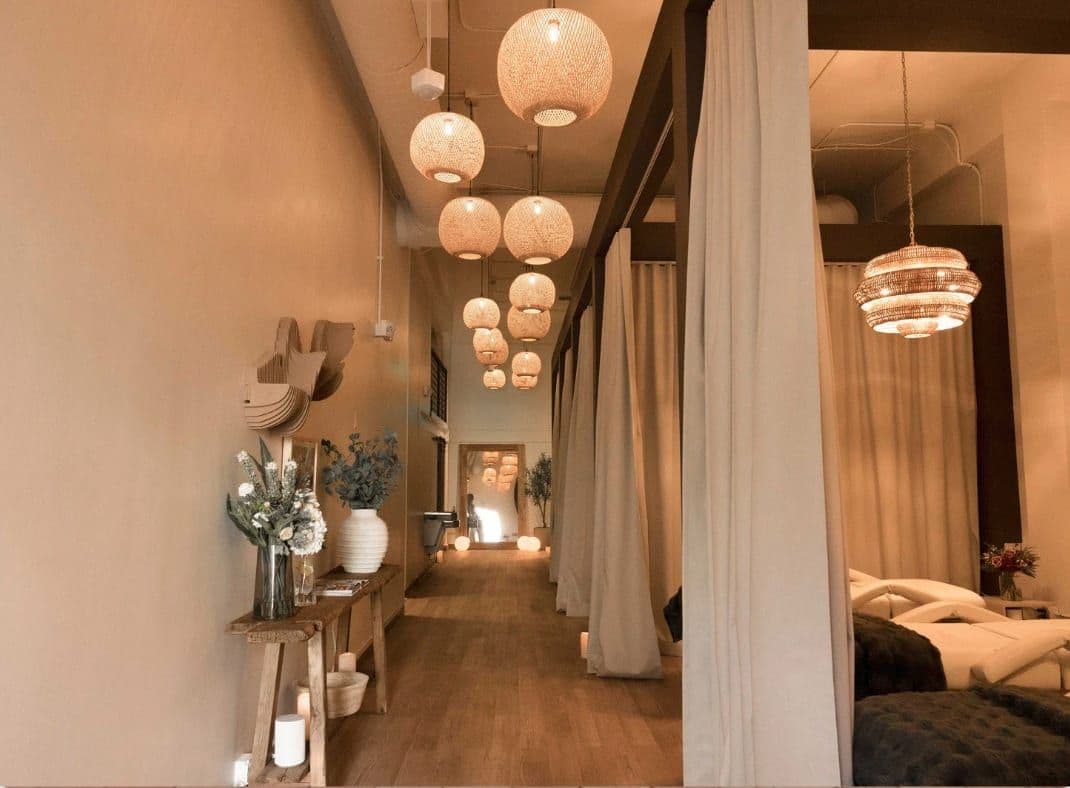 Modern spa corridor with woven pendant lights and cream drapes leading to treatment rooms