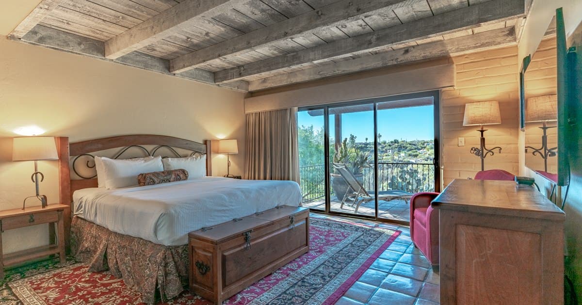 Bedroom with bed, nightstands, exposed beam ceiling, and balcony overlooking hillside landscape