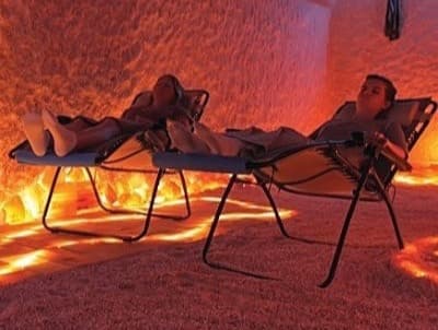 Two people relaxing in lounge chairs inside a salt cave with glowing amber lighting