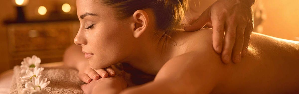 Woman receiving a relaxing shoulder and neck massage with warm lighting and flowers