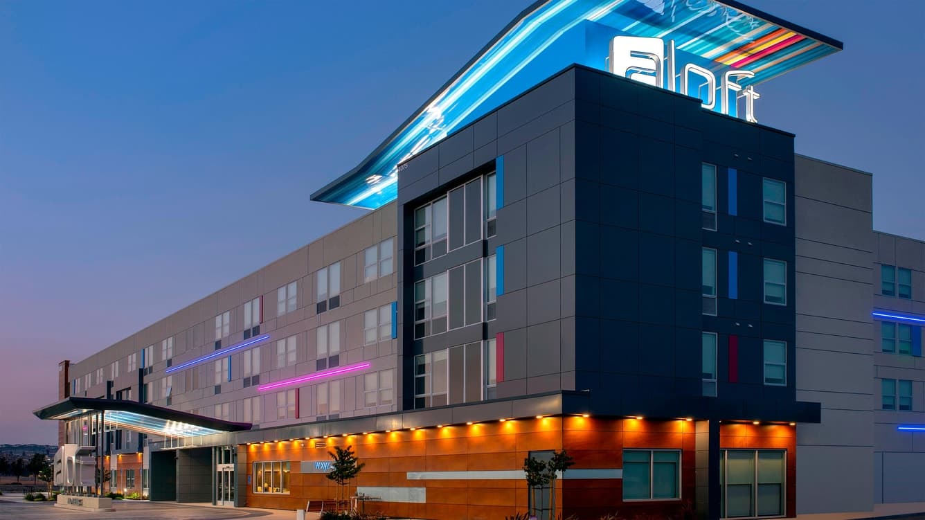 Modern hotel exterior at dusk with illuminated neon signage and glass windows