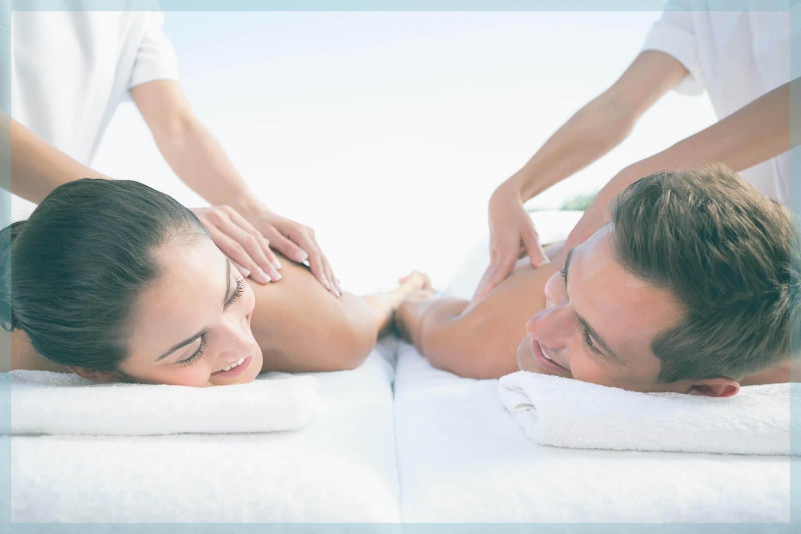 Couple receiving back massage on white sheets with spa therapists' hands visible