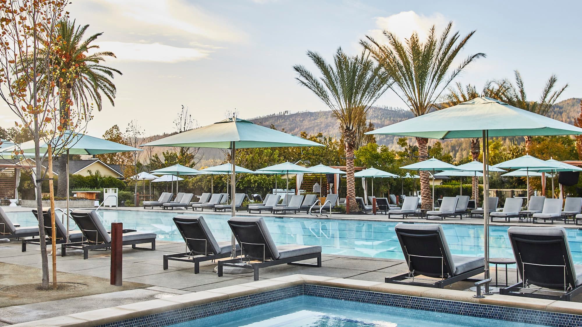 Resort pool with lounge chairs, umbrellas, and mountain views